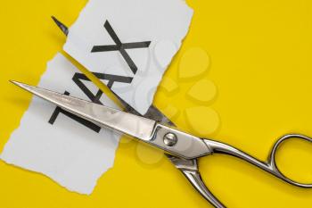 Scissors and printed paper with the word tax on it cut in half. Tax cuts concept