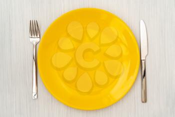 Empty yellow plate with fork and knife. View from above.