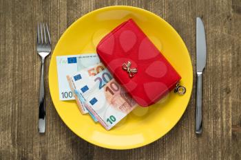 Savings consumer concept.Red wallet on the yellow plate with fork and knife.
