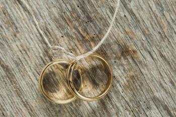 Two gold wedding rings tied with string over wood background