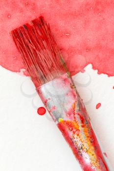 Paintbrush and splatter of red watercolor on white paper. Close-up view.