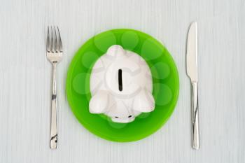 Savings consumer concept. Piggy bank on the green plate with fork and knife