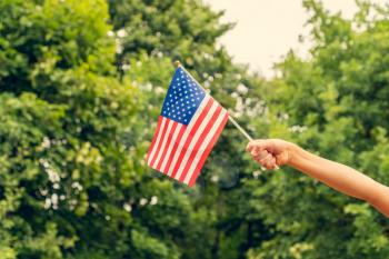 Child's hand with american flag outdoors on summer day. Independence Day concept.