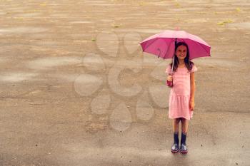Child girl wearing  rain boots standing on wet asphalt