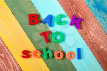 Sentence Back to school in colorful plastic letters over color wooden background