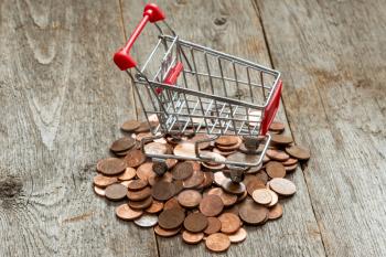  Consuming concept with shopping cart and euro cents on wooden background