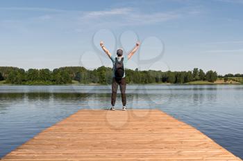 Young man standing on a pier with raised hands