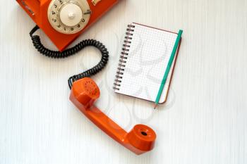 Vintage orange telephone and blank notebook on wooden background, top view, pick up the phone