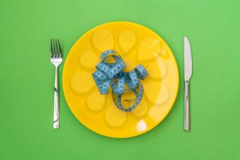  The concept of starvation or diet. Plate with knife, fork and measure tape on green background