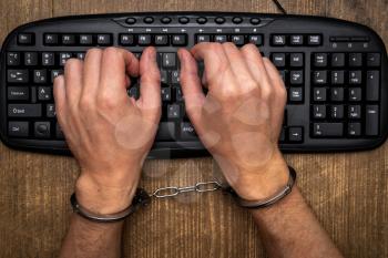 Hacker concept, punishment for cybercrime with hands in handcuffs above computer keyboard