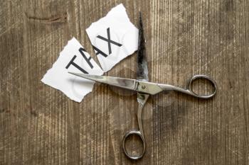 Scissors and printed paper with the word tax on it cut in half. Tax cuts and reform saving people money concept