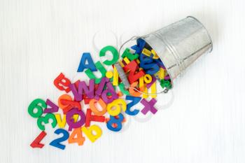 Colorful plastic numbers and letters falling from metal bucket