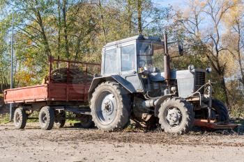 Tractor with a trailer filled with tree branches and dead leaves in the city park in autumn day