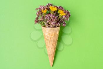 Flowers in a waffle cone on a green background. Flat lay, top view.