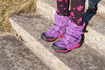 Little girl with winter shoes standing on the old stone stairs