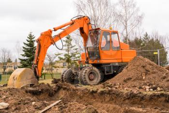 An orange excavator digging a trench for city communications