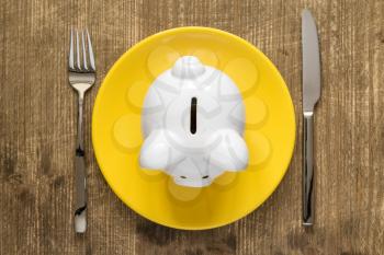 Savings consumer concept. Piggy bank on the plate with fork and knife. 
