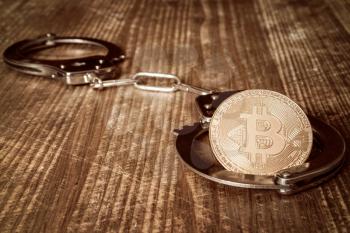 Golden bitcoin and handcuffs on wooden table