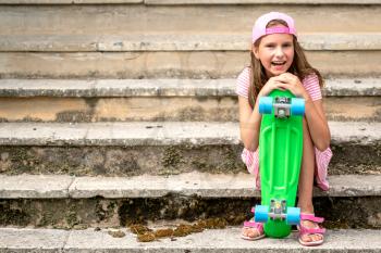 Little girl child with skate board sits on the stair