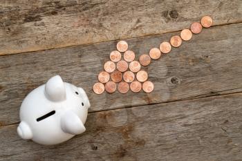Coins arranged as a arrow showing to piggy bank. Financial savings concept.