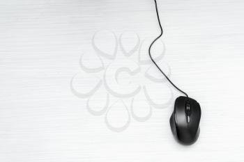 Simple black computer mouse with cord on wooden background, top view