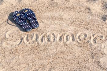 Flipflops on beach, with the word summer written on sand