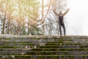 Man standing on the top of mossy stairs and raising hands up. Unrecognizable rear view.