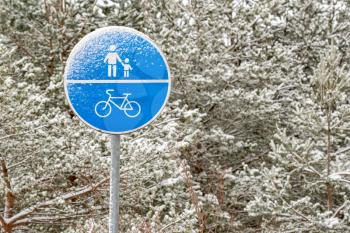 Snow covered sign of a bike path and a pedestrian in the park in winter