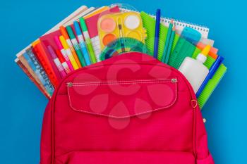 Back to school concept. Backpack with school supplies on the blue background.