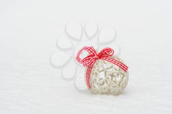 Christmas bauble with a red bow on the white fresh snow. Copy space.