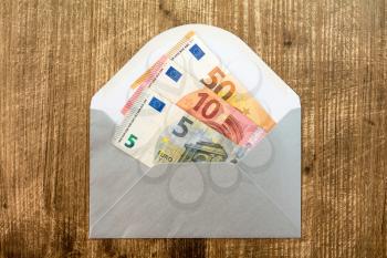 Silver envelope with Euro currency over wooden background