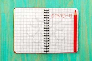 Text COVID-19 with red pencil on a spiral notebook. Conceptual image of corona virus outbreak.