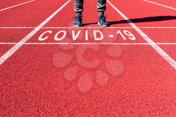 Win against virus. Athlete at the sprint start line in track with text COVID-19