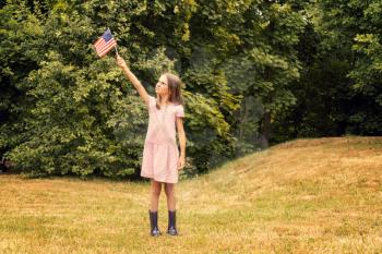 Child girl with small american flag stands in park
