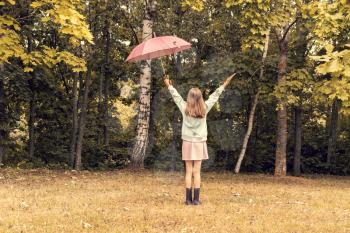 Child girl with umbrella stands against park trees