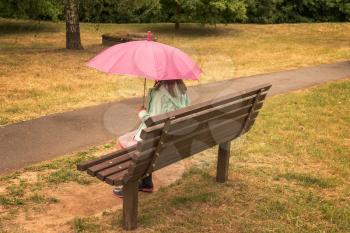 Girl under umbrella sitting on bench in park