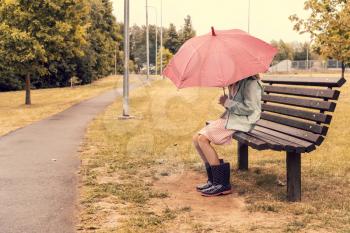 Girl with umbrella sitting on bench in park