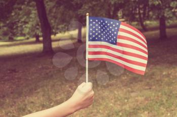  Child waving US flag on the park background. Filtered image.