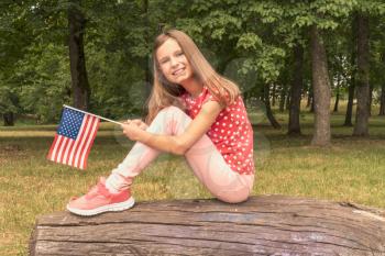 Happy girl with small american flag sits at park