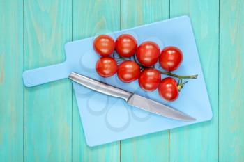 The branch of tomatoes and knife on a blue cutting board