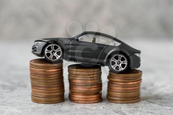 Money saving for a car. Coin stacks with a car on grey background