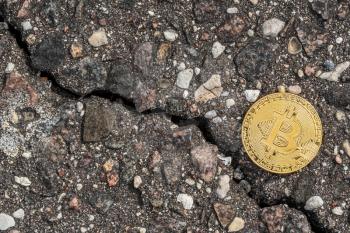 Shiny golden bitcoin on cracked pavement. Crack goes down as cryptocurrency crash concept