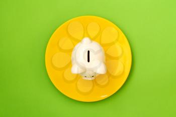 Savings consumer concept. Yellow plate with piggy bank on green background