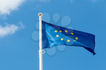 A flag of european union is waving on a background of blue sky with white clouds