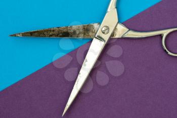  Metal scissors on purple and blue paper background