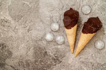 Chocolate ice cream in wafer cone and ice pieces on grey background