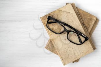 Eyeglasses on stacked books placed on white wooden background. Top view, copy space.