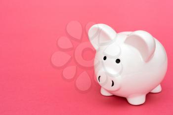 White piggy-bank on pink background, copy-space