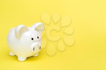 White piggy-bank on yellow background, copy-space
