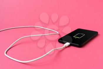Black mobile smart phone with a charger on pink background
